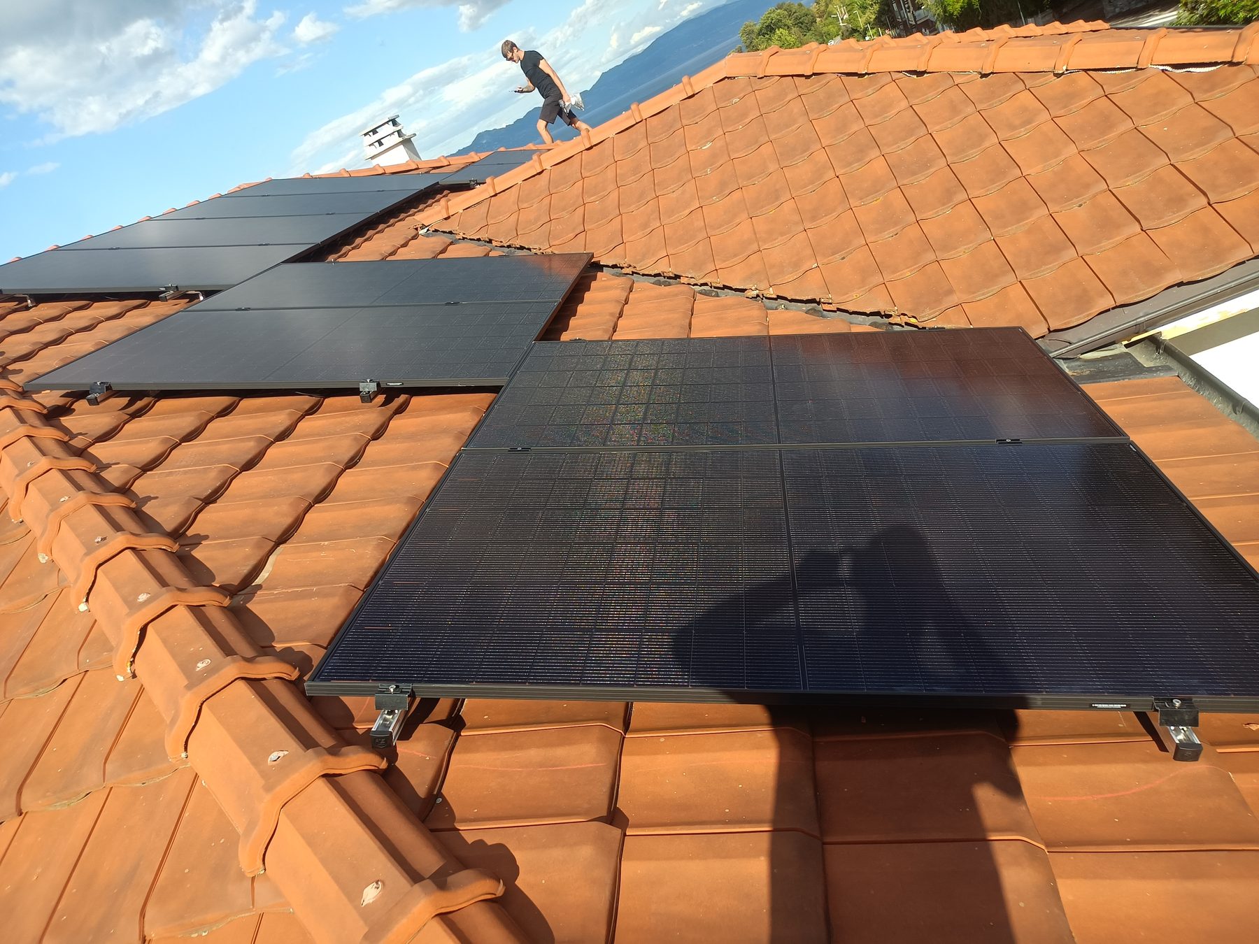 Installation de panneaux solaires par L2B ENERGIES sur une toiture en tuiles, face au lac et aux montagnes